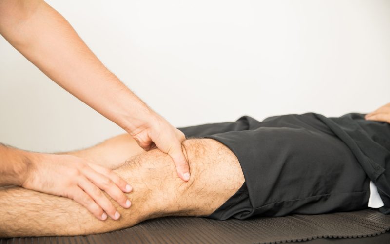 Hands of physiotherapist applying pressure to massage young man's knee in hospital